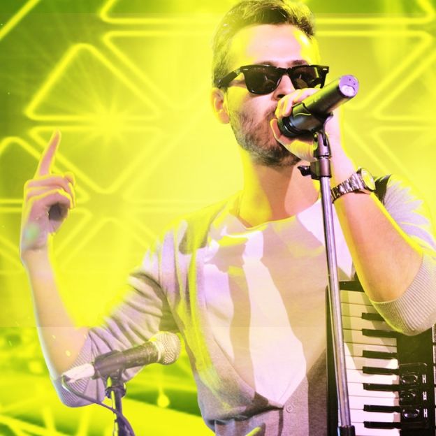 Cantor Edward Maya canta com a mão direita apontada para cima no centro da imagem